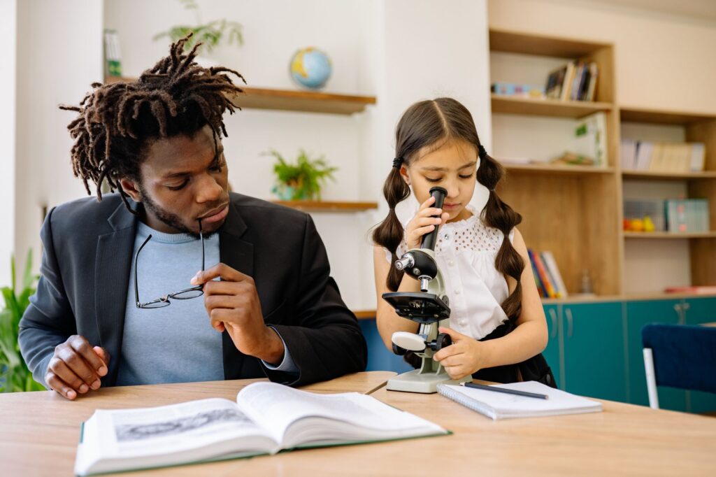 A teacher guides a student looking through a microscope