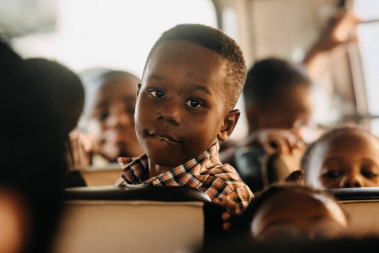 A young boy on a school bus gazes thoughtfully ahead, s